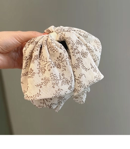Détail d'une pince à cheveux en mousseline fleurie avec nœud en tissu crème et brun