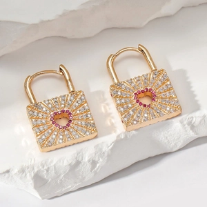 Detail of gold square lock earrings with pink heart rhinestones on stone background
