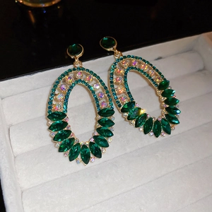 Macro shot of luxurious oval drop earrings with emerald green crystals and sparkling rhinestones