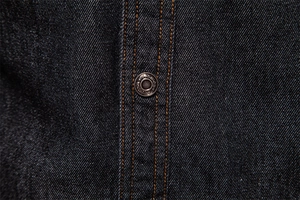 Détail d'une chemise en denim délavé avec coutures orange et boutons métalliques gravés