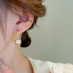 Gros plan de boucles d'oreilles carrées dorées avec perle blanche portées par un mannequin