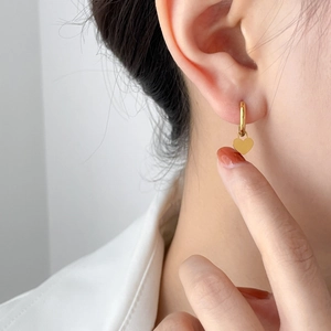 Close-up of a minimalist golden heart charm earring worn on ear with polished finish