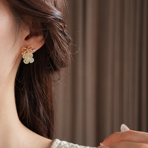 Detailed view of model wearing gold bow floral earrings with mother of pearl and pearls