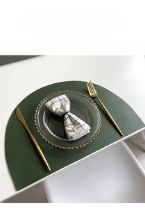 Detail of dark green PU leather placemat with fine texture and gold cutlery on table