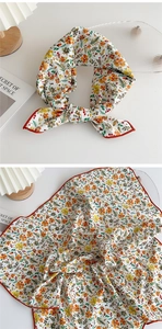 Detailed view of square silk scarf with vibrant floral patterns and red stitched edges
