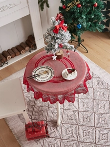 Detail of red lace Christmas tablecloth with festive tree and fireplace decor