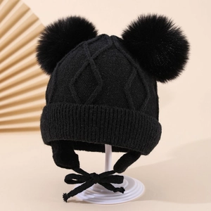 Close-up of black diamond knit earflap hat for kids with fluffy double pom-poms and straps