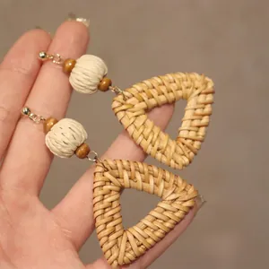 Macro detail of handmade bohemian woven rattan triangle earrings with wooden beads