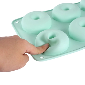 Flexible light green 6-cavity silicone donut mold being pressed to show soft texture