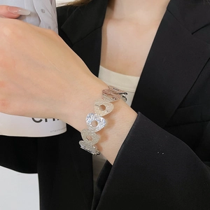 Detail of silver heart-shaped chain bracelet with hammered texture on a woman's wrist