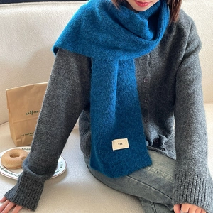 Detailed close-up of blue knit scarf featuring a soft texture and minimalist egg woven label