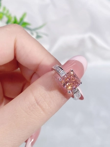 Close-up of a silver ring featuring a square orange-pink stone and clear side gems