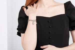 Close-up of double-layered silver chain bracelet with oval medallion on female wrist