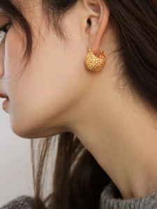 Macro detail of French style gold hollow ball earrings with honeycomb texture pattern