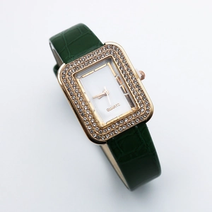 Detail of square gold watch face with crystal rhinestones and green leather strap