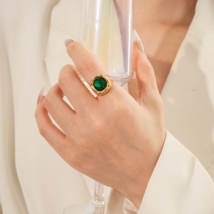 Dettaglio anello vintage oro con zircone verde smeraldo indossato da modella con bicchiere