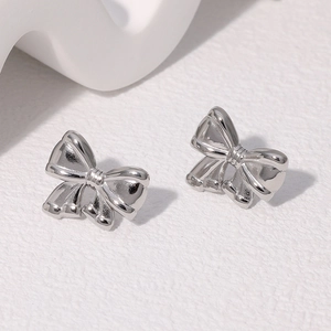 Gros plan de boucles d'oreilles nœuds en acier argenté sur fond texturé beige