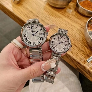 Pair of silver stainless steel watches with Roman numerals on a wooden table setup