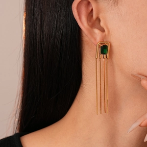 Close-up of elegant gold tassel earrings with green zircon on a model's ear