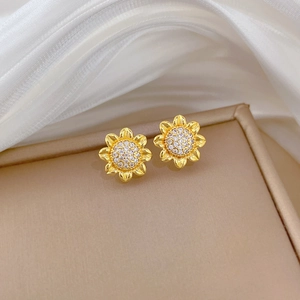 Close-up of golden sunflower stud earrings with sparkling crystals on silk fabric