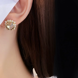 Close-up of golden champagne crystal halo stud earrings worn on a female model