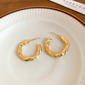 Detail of C-shaped gold-tone hoop earrings with hammered texture and cubic zirconia