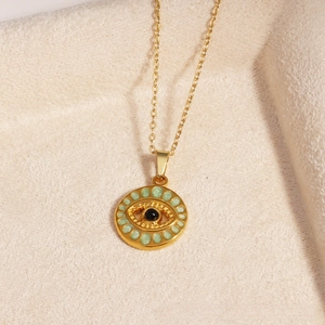 Macro detail of gold devil eye pendant with green enamel and black center bead on o-chain