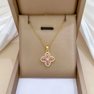 Macro view of gold clover pendant with pink gemstones and pavé diamonds in a jewelry box