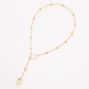 Macro detail of golden bead chain necklace with hollow heart and letter S pendant
