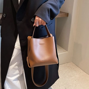 Close-up of a brown leather bucket bag featuring a top handle and logo detail