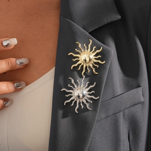 Detail of geometric sun-shaped metal brooches in gold and silver on grey blazer lapel