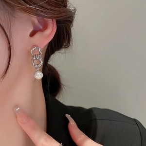 Close-up of model wearing silver chain earrings with portrait coin and pearl drop
