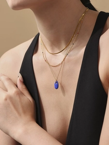Nahaufnahme einer dreilagigen goldenen Halskette mit einem marineblauen Emaille-Anhänger