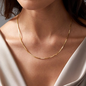 Detailed view of a gold box chain necklace worn on the neck to show length and luster