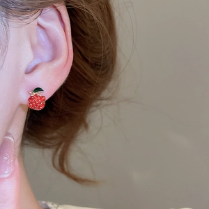 Close-up of sparkling red apple crystal earrings on ear with gold metal leaf detail