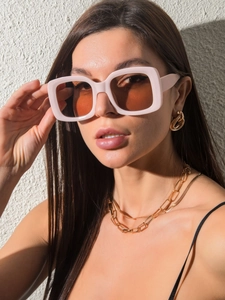 Detail of pink square sunglasses with brown lenses and golden jewelry on female model