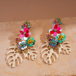 Detailed shot of oversized floral sequin earrings with white monstera leaf pendants