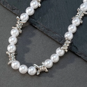 Detailed close-up of a silver cross pendant with faux pearls on dark stone