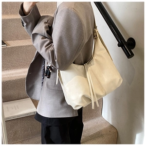 Side view of cream leather tote bag worn by a model in a minimalist indoor setting