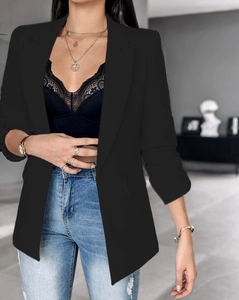Detalle de un blazer negro de manga larga con solapas sobre un top de encaje negro