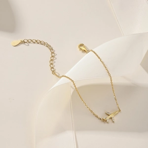 Close-up of a gold S925 sterling silver airplane charm bracelet on white silk ribbon