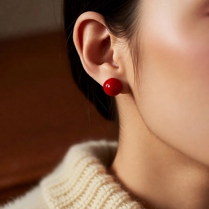 Close-up of minimalist red spherical stud earrings worn by a model in beige knitwear