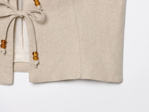 Detail of beige cotton linen vest with amber beads on the decorative tie closure