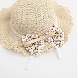 Detail of kids straw sun hat with floral bow and white scalloped lace trim details