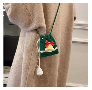 Detail of green knit Christmas crossbody bag with red bow and yellow bell on model