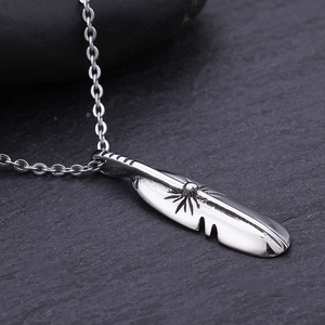 Detailed close-up of a silver feather pendant showing fine textures on dark stone