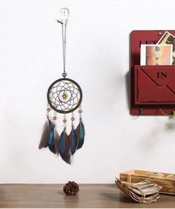 Close-up of a handmade dreamcatcher with dark blue feathers and gold beads on a white wall
