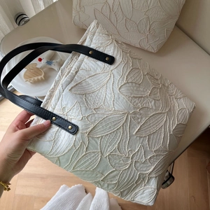 Macro detail of leaf-patterned quilted embroidery and leather strap on beige tote bag