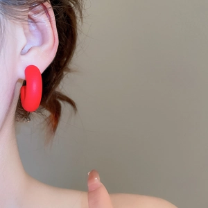 Close-up detail of a minimalist matte wine red C-shaped acrylic earring on a model