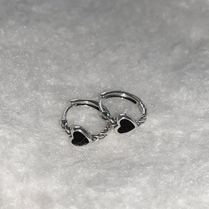 Silver heart earrings with black enamel and twisted texture on a white plush background